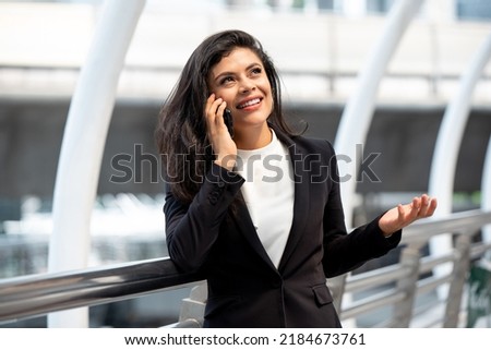 Smiling young Hispanic business woman talking on mobile phone outdoors in the city