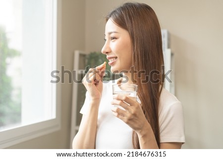 Dietary supplement, asian young woman, girl hand holding orange medical pill, take or eat vitamin C, D for treatment for skin, hair and nail strengthen with glass of pure water at home, healthcare. Royalty-Free Stock Photo #2184676315
