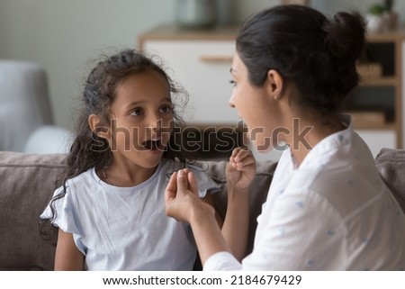 Indian female therapist training kid with hearing disability, deafness to use fingers for communication. Mom and cute daughter kid speaking sign language, talking, using hand gestures Royalty-Free Stock Photo #2184679429