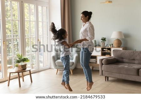 Excited Indian kid and happy mom holding hands, jumping to music on floor. Cheerful mother teaching kid to dance music in living room, smiling, laughing, having fun. Family activity concept Royalty-Free Stock Photo #2184679533