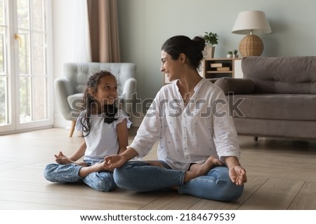 Happy Indian mom and kid girl enjoying yoga at home, sitting in lotus pose on heating floor, keeping zen fingers, talking, laughing, smiling. Mother teaching little daughter to meditate at home Royalty-Free Stock Photo #2184679539