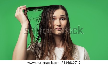 Attractive young woman is sad about her dirty, oily and greasy hair, isolated on a green background. Need a shampoo concept. Easily removable and replaceable chroma key background. Royalty-Free Stock Photo #2184682719
