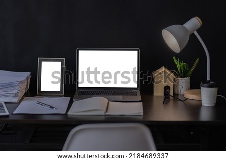 Laptop Computer blank screen on wood table, notebook, and eyeglasses sitting on a desk in a large open plan office space after working hours