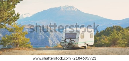 Caravan trailer parked on a mountaintop with a view on French Alps near lake Lac de Serre-Poncon. Transportation, RV, motorhome, road trip, camping, tourism, recreation, lifestyle Royalty-Free Stock Photo #2184695921