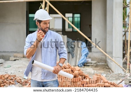 Single Foreman hold blueprint and use walkie talkie to hear team speaking in village construction site