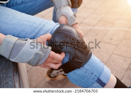 Pads and knee pads. Woman rollerskater putting on knee protector pads on her leg. Equipment for safety for rollerskater. Safety accessoryes for skating. Royalty-Free Stock Photo #2184706703