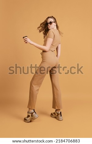 Happy girl, student listening to music and dancing isolated over brown color background. Concept of beauty, art, fashion, youth, sales and ads. Blonde looks happy, excited. Copy space for ad