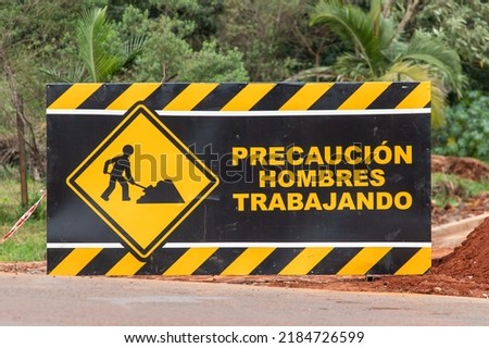 sign that says "caution men working" in Spanish