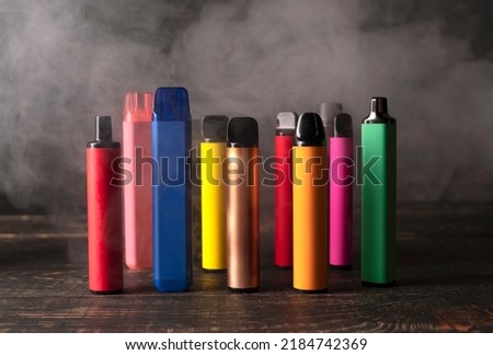 Set of colorful disposable electronic cigarettes on a dark wood background with smoke. The concept of modern smoking, vaping and nicotine. Royalty-Free Stock Photo #2184742369