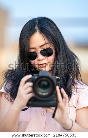 Amateur sunglasses Asian Woman take a photo with professional mirrorless camera at outdoor blue rooftop building in twilight time.