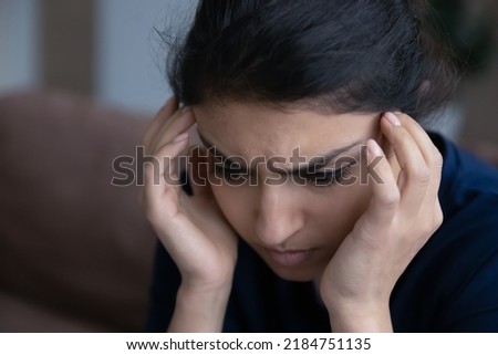 Close up of sad millennial Indian woman suffer from migraine or headache at home. Unhappy unhealthy young mixed race female struggle with depression, feel anxiety. Outcast, loneliness concept. Royalty-Free Stock Photo #2184751135