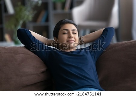 Calm millennial Indian woman rest on comfortable couch in living room sleep or take nap on weekend. Happy young mixed race female relax on sofa at home daydream. Relaxation, stress free concept. Royalty-Free Stock Photo #2184751141