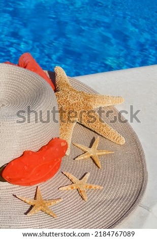 Women's hat decorated with starfish on the background of a blue pool. On a bright summer day.