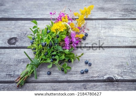 Lovely bouquet of bilberry branches and colorful wildflowers on wooden table with some berries scattered around. Royalty-Free Stock Photo #2184780627