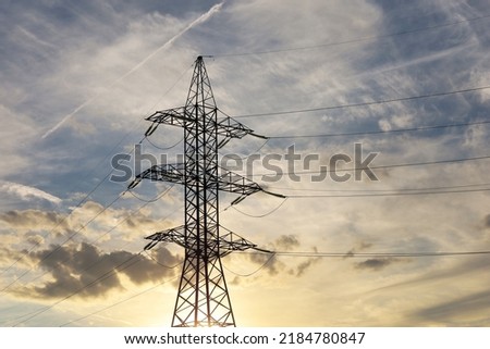 Silhouette of high voltage tower with electrical wires on background of sunset sky and clouds. Electricity transmission lines, power supply concept