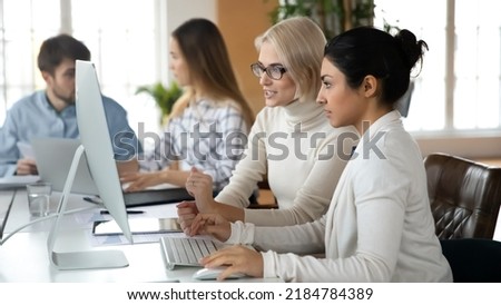 Focused multiracial businesspeople sit at desk in office look at PC screen brainstorm discussing company financial ideas or project. Serious diverse female employees cooperate using computer Royalty-Free Stock Photo #2184784389