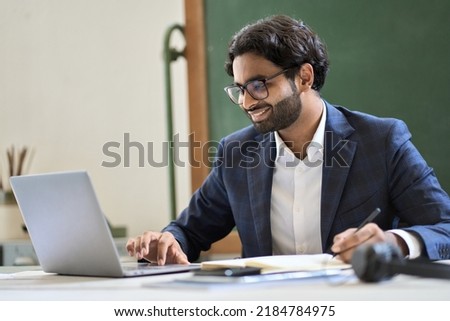 Happy arabic indian young business man executive manager, office employee or teacher wearing suit working on laptop computer, online learning teaching on professional webinar, doing market research.
