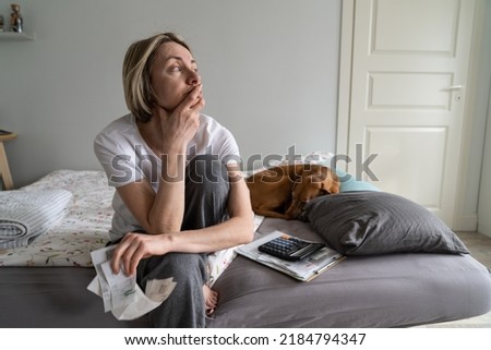 Single depressed mature woman widow loses life sense and motivation. Middle-aged blonde female wearing nightwear sits on bed holding hand on chin looking in distance and waiting for help closeup Royalty-Free Stock Photo #2184794347