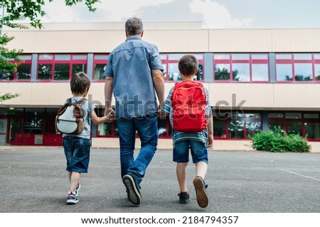 Back to school. View from the back of a happy dad escorts his sons schoolchildren to school. Parental care for children Royalty-Free Stock Photo #2184794357