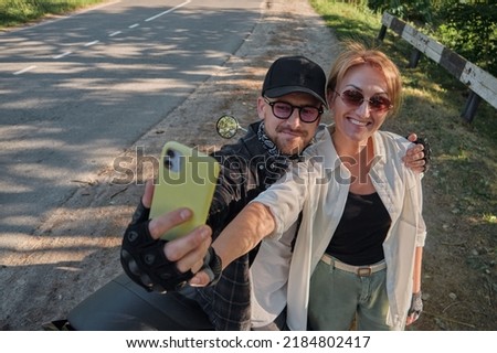 Middle age couple riding a motorcycle having fun and taking a selfie on a mobile phone camera