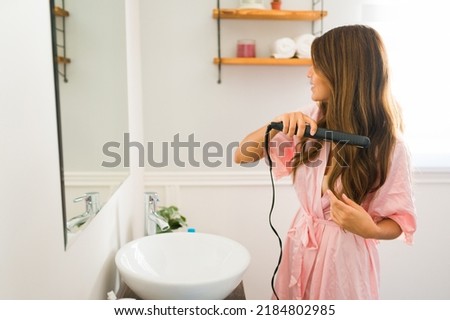 Profile of a beautiful woman with long hair using a hair iron and doing a hairstyle to go out in the morning Royalty-Free Stock Photo #2184802985