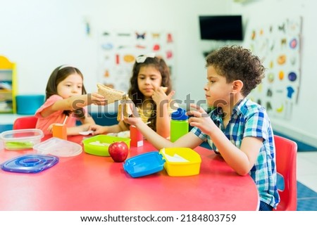 Little children and preschool friends sharing their food while eating a sandwich and healthy snacks during lunch break at school  Royalty-Free Stock Photo #2184803759