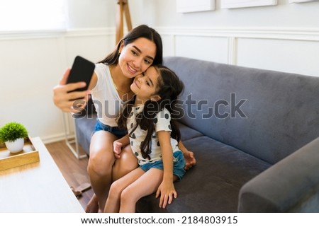 Beautiful mother and little kid smiling and hugging while taking a selfie together with a smartphone to post it on social media 