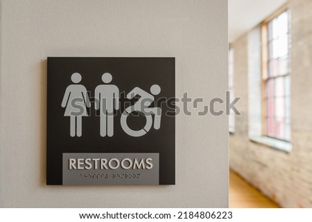 Close-up of unisex bathroom sign against neutral colored wall with symbols for male, female, and wheelchair. Copy space.