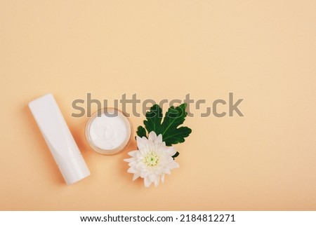 Natural cosmetics cream jar and tube, white dahlia flower on beige background. Top view, flat lay, copy space.
