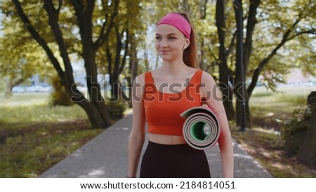 Athletic fitness sport runner girl walking with sport yoga mat to do fitness stretching exercises. Young woman training cardio workout in park at morning. Active sportswoman. Aerobic, weight loss