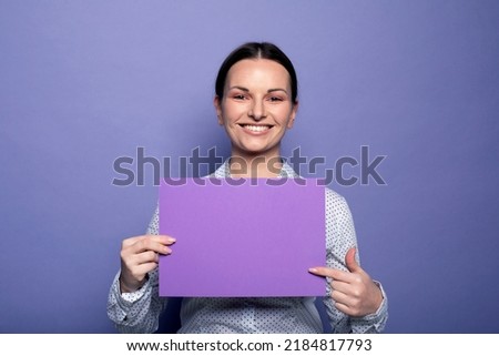 Fashion and beauty concept: Young business woman holding purple blank advertising board standing on lilac background in studio