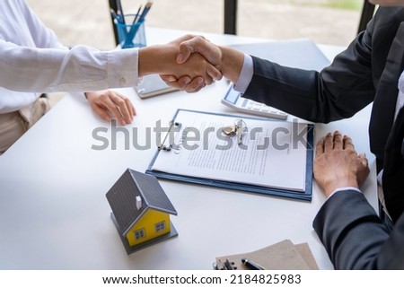 The estate agent and client are shaking hands after a good deal home loan after discussing and signing a contract to rent a house with an approved insurance form