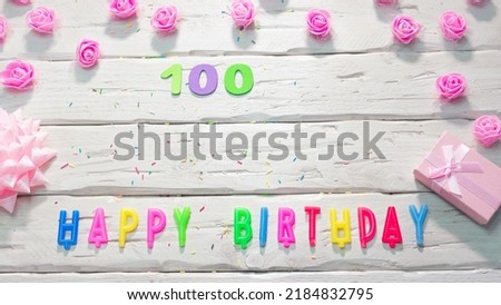 Top view of happy birthday candle letters for a girl in pink shades with beautiful rose flowers, postcard congratulation copy space on wooden boards. Beautiful birthday card number 100