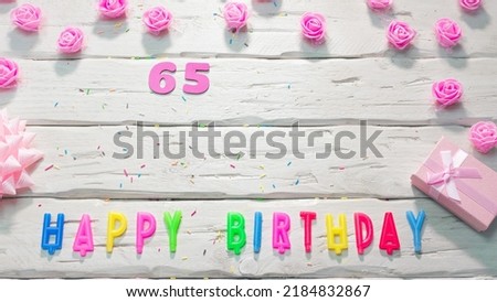 happy birthday candle letters for a girl in pink shades with beautiful rose flowers, postcard congratulation copy space on wooden boards. Beautiful birthday card number 65