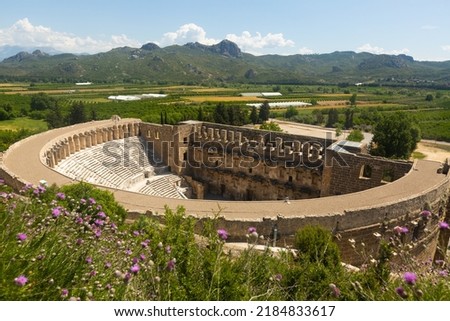 Scenic view of well-preserved Roman theater, main attraction of ancient Greco-Roman city of Aspendos on background of surroundings with green agricultural fields and mountain range in spring, Turkey Royalty-Free Stock Photo #2184833617
