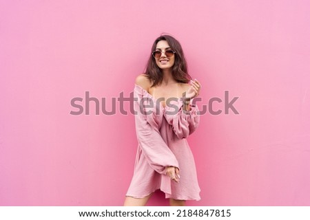 Young beautiful smiling cute romantic woman in trendy summer dress. Carefree woman posing in the street near pink wall. Positive model outdoors in sunglasses. Cheerful and happy
