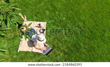 Young woman using laptop computer in park, student girl freelancer working and studying online outdoors sitting on grass with headphones and laptop, aerial drone view from above Royalty-Free Stock Photo #2184860395