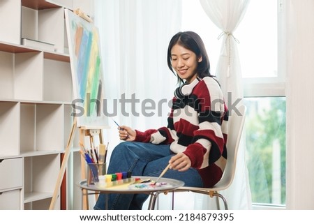 The art concept, Asian female artist smiling to happy while using brush to dip in color palette.