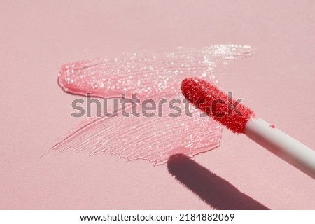 Smears of shining lip gloss and lip gloss brush on pink background, hard shadows Royalty-Free Stock Photo #2184882069