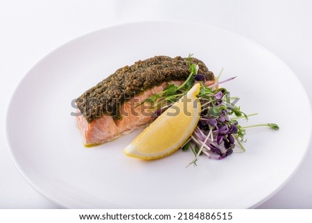 Fried salmon steak with young shoots of green peas, lemon on a white round plate. Horizontal
orientation
