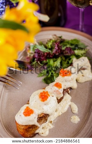 Fried piece of salmon with red caviar, salad, arugula and thyme sauce on a plate with table pibors, flowers and a glass of wine. Vertical orientation