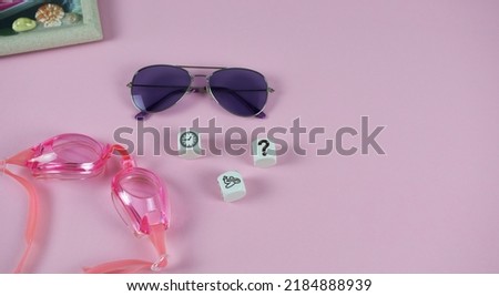 Pink background sunglasses, with picture frame, goggles , cubes with airplane, clock and question mark. A beautiful layout on the theme of planning a family vacation. 