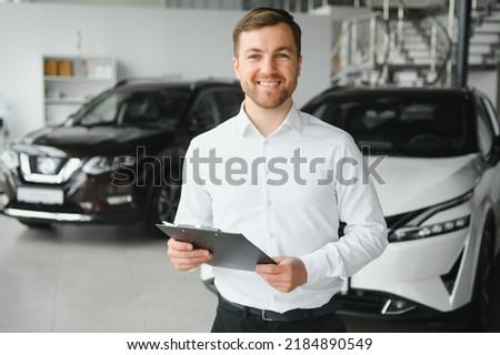 Assistant in vehicle search. Portrait of a handsome young car sales man in formalwear holding a clipboard and looking at camera in a car dealership. Royalty-Free Stock Photo #2184890549