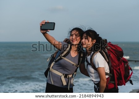 Backpack travel concept, two beautiful Asian female backpackers Taking a selfie using a smartphone.