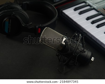 A studio microphone, studio headphones and a modern synthesizer-midi keyboard on a dark gray background. The concept is a recording studio, a music studio.