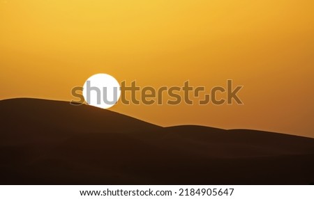 Gold yellow sunset with circular full round sun ball touching silhouette of desert sand dunes sky, copy space - Morocco, Sahara Erg Chebbi, North Africa Royalty-Free Stock Photo #2184905647