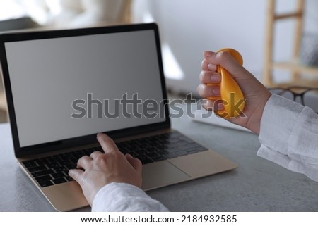 Woman squeezing antistress ball while working on laptop in office, closeup