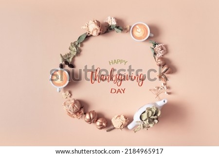 Autumn composition with Happy Thanksgiving Day greeting text. Wreath made of dried leaves and coffee cups on pastel beige background.