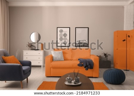 Stylish living room interior with orange sofa, armchair and beautiful pictures