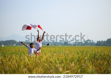 Indonesian school students wearing uniform are raising their hands while holding red white flag in the midst of the rice field. Celebrating independence day. Royalty-Free Stock Photo #2184972957